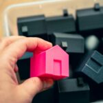 A person holding a pink house in front of a pile of black cubes
